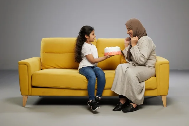 Saudi Mother and Daughter with Cake on Yellow Sofa