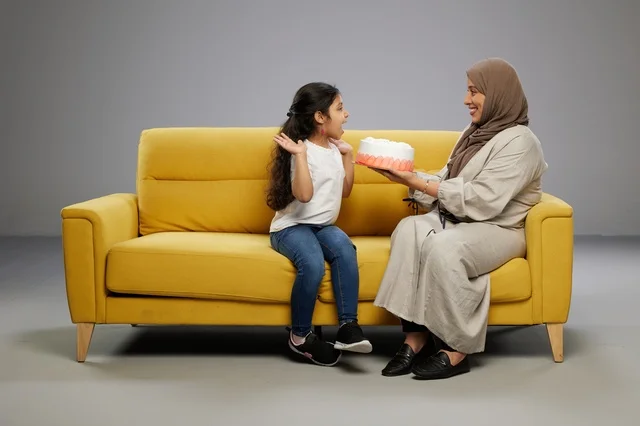 Arab Mother and Daughter with Cake on Yellow Sofa