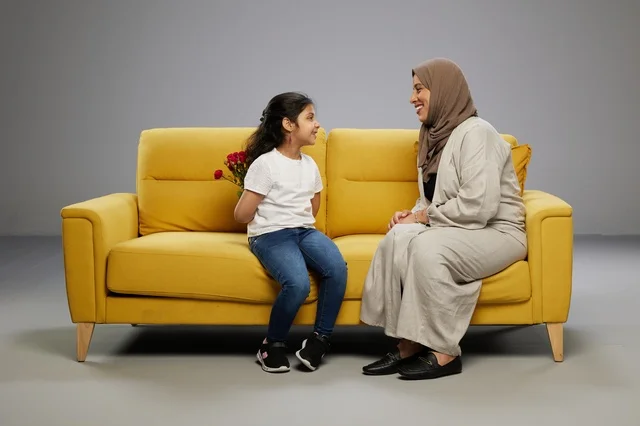 طفلة تخفي الزهور خلف ظهرها لوالدتها على الأريكة