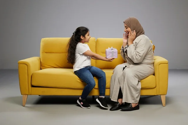 أم عربية وابنتها مع هدية على أريكة صفراء