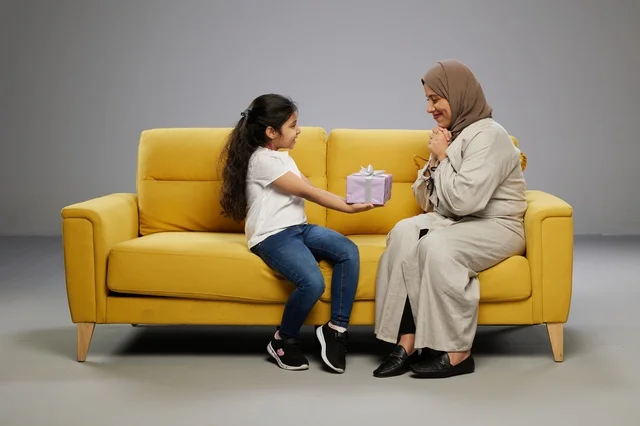 أم وابنة عربية مع هدية على أريكة صفراء