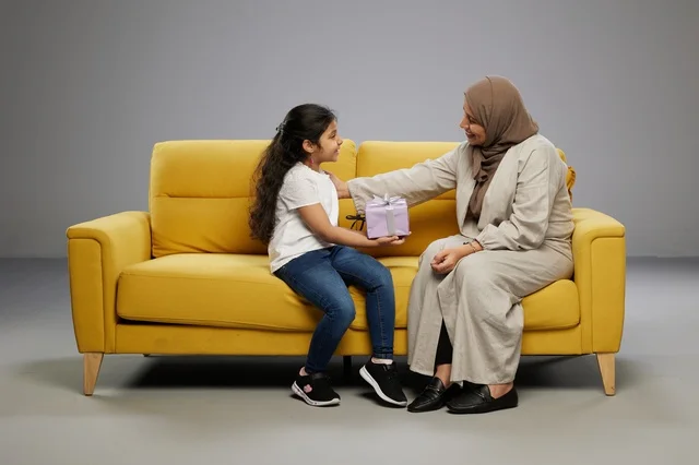 أم عربية تقدم هدية لابنتها على أريكة صفراء