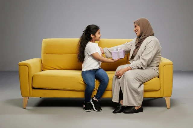 أم عربية تقدم هدية لابنتها على أريكة صفراء