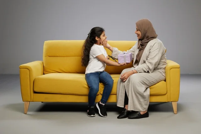 Saudi Mother Giving Gift to Daughter on Yellow Sofa