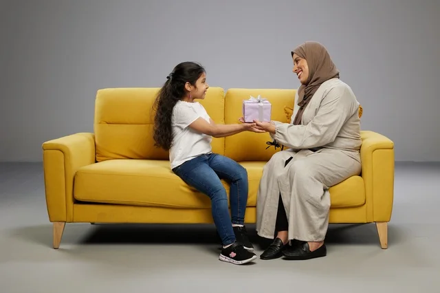 Saudi Mother Giving Gift to Daughter on Yellow Sofa