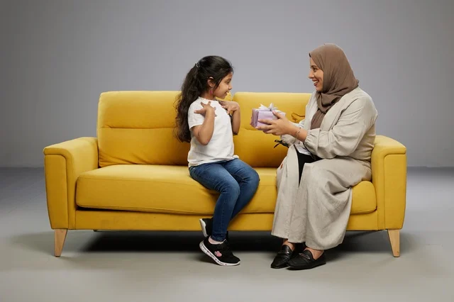 أم عربية تقدم هدية لابنتها على أريكة صفراء أم عربية تقدم هدية لابنتها على أريكة صفراء