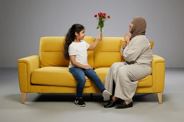 طفلة تقدم زهور حمراء لوالدتها على أريكة صفراء