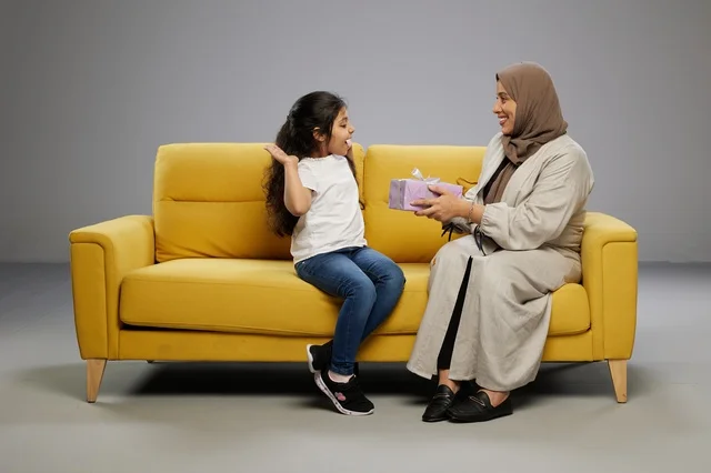 أم عربية تقدم هدية لابنتها على أريكة صفراء أم عربية تقدم هدية لابنتها على أريكة صفراء