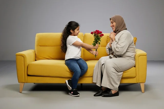 فتاة عربية تقدم ورود حمراء لوالدتها على أريكة صفراء