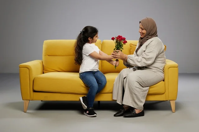 فتاة عربية تقدم ورد أحمر لوالدتها على أريكة صفراء