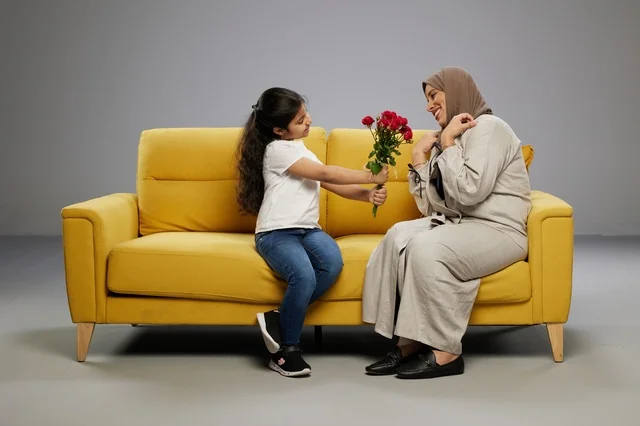 طفلة عربية تقدم ورد أحمر لوالدتها على أريكة صفراء