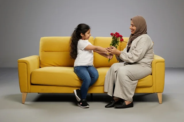 فتاة عربية تهدي زهور حمراء للأم على أريكة صفراء