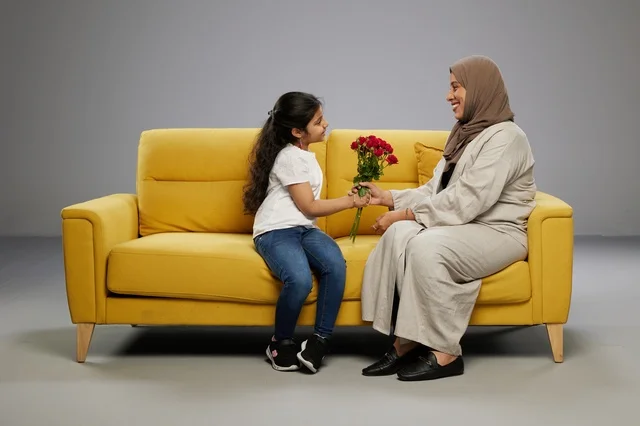 طفلة عربية تقدم الزهور لوالدتها على أريكة صفراء