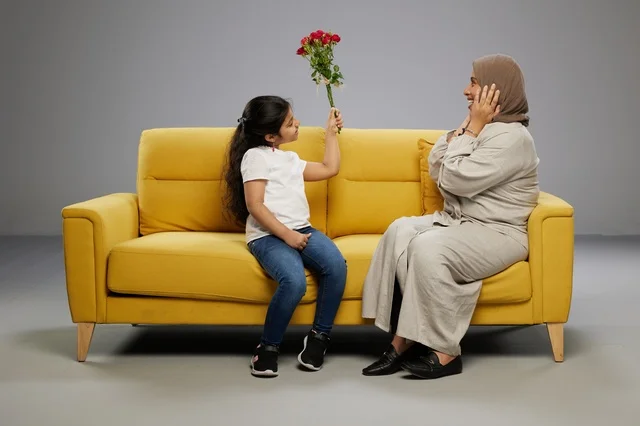 أم عربية وابنتها مع ورد على أريكة صفراء