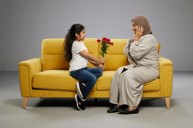 Arab Girl Gifting Red Roses to Mother on Yellow Sofa