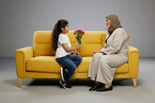 طفلة عربية تهدي زهور حمراء لوالدتها على أريكة صفراء