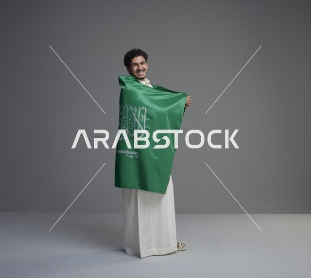 شاب سعودي يلتف بالعلم الوطني السعودي في الاستوديو