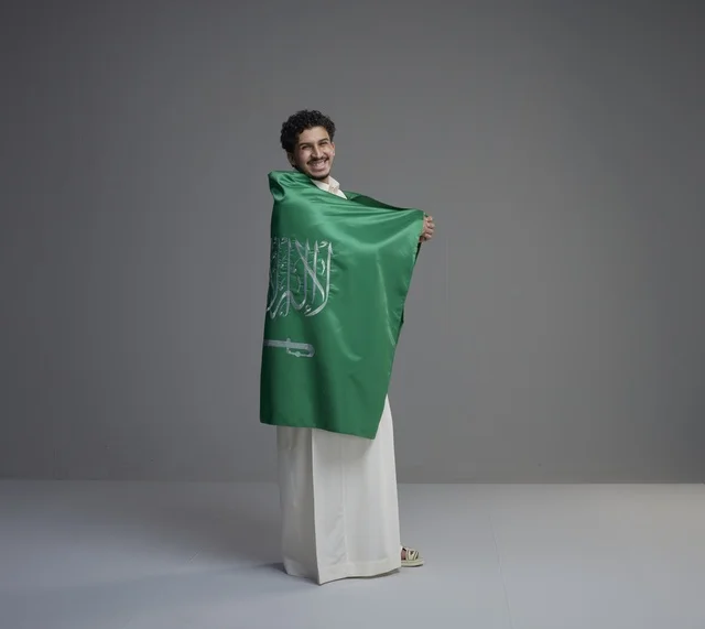 شاب سعودي يلتف بالعلم الوطني السعودي في الاستوديو