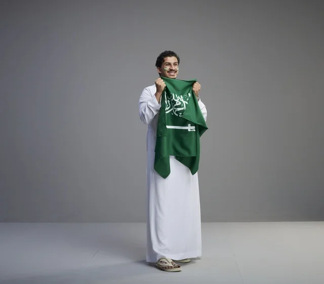 شاب سعودي بالثوب التقليدي يحمل علم المملكة
