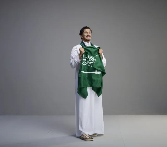 شاب سعودي مبتسم يحمل العلم الوطني في الاستوديو