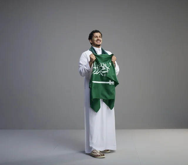 شاب سعودي يمسك العلم الوطني بخلفية رمادية