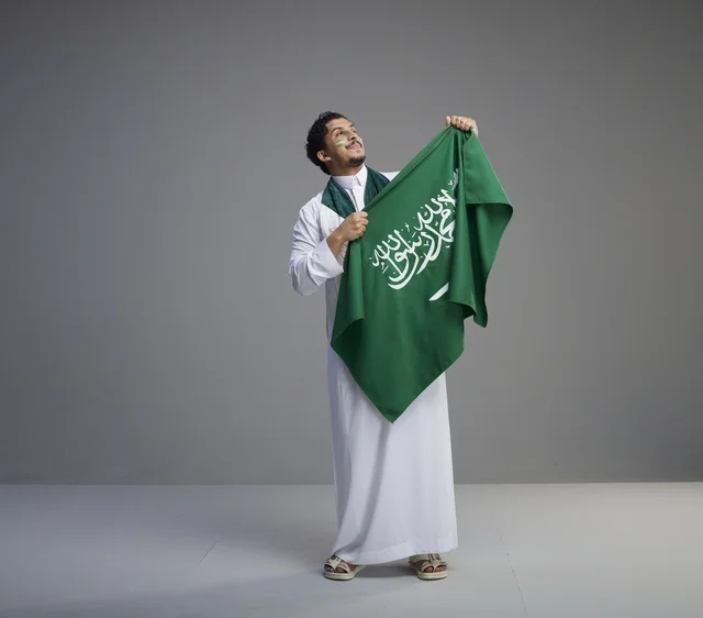شاب سعودي يبتسم ويحمل العلم الوطني في الاستوديو