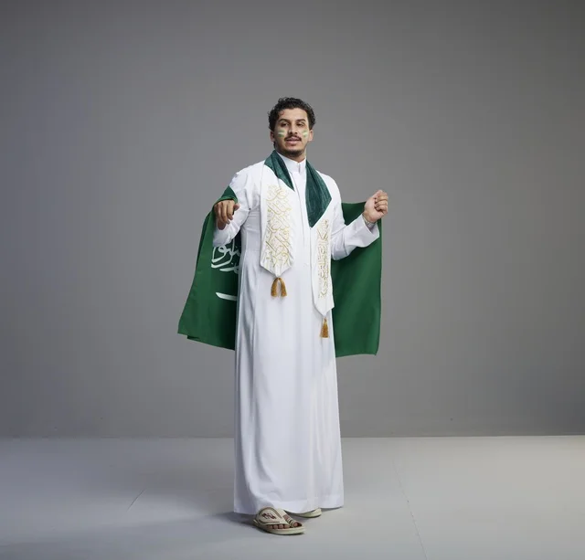 شاب سعودي مبتسم يحمل العلم الوطني في الاستوديو