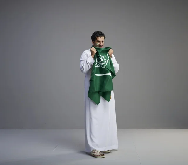 شاب سعودي مبتسم يحمل العلم الوطني في الاستوديو