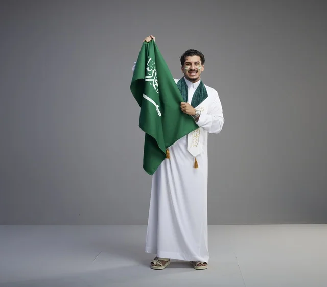 شاب سعودي يمسك العلم الوطني بخلفية رمادية