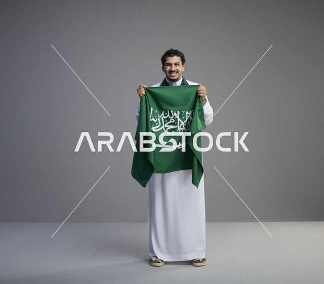 شاب سعودي مبتسم يحمل علم المملكة العربية السعودية