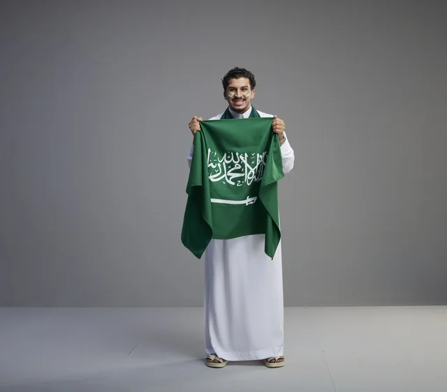 شاب سعودي مبتسم يحمل علم المملكة العربية السعودية