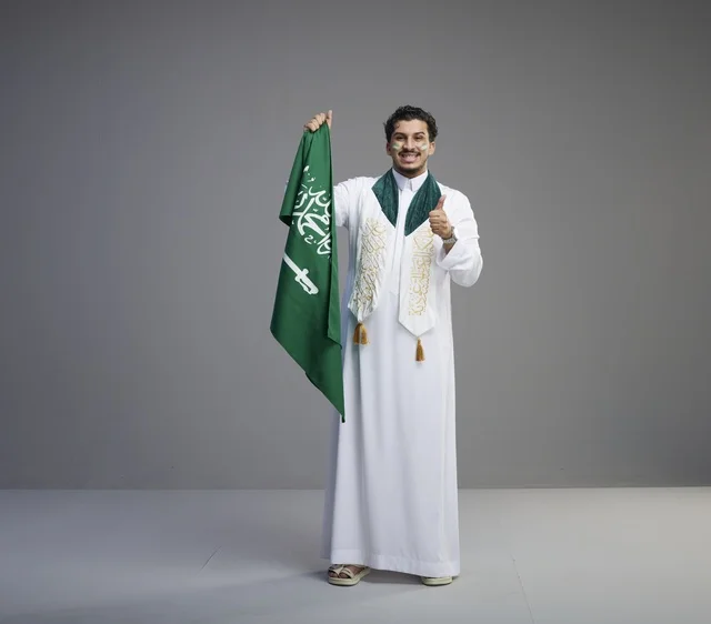 شاب سعودي يحمل العلم الوطني السعودي مع إشارة الإعجاب