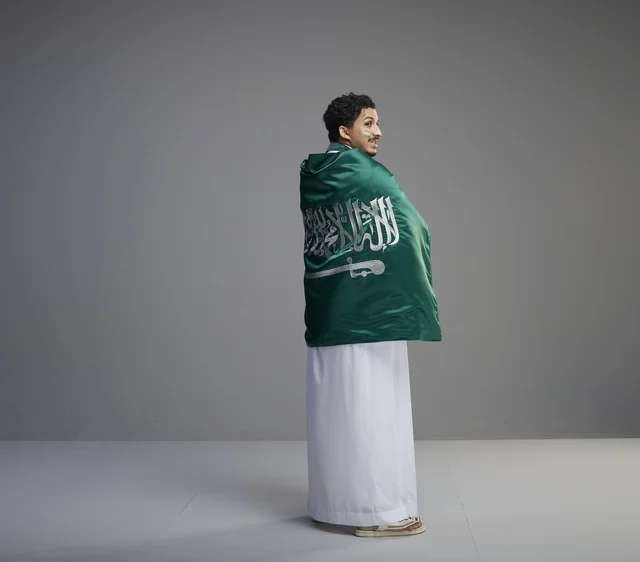 شاب سعودي يلتف بالعلم الوطني السعودي في استوديو تصوير