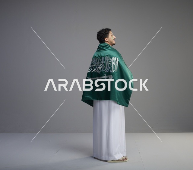 شاب سعودي يرتدي الثوب ويلتف بعلم المملكة