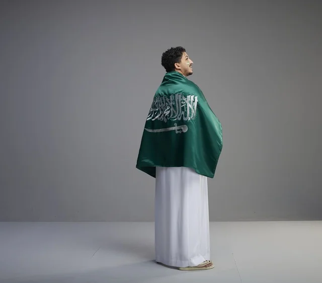شاب سعودي يرتدي الثوب ويلتف بعلم المملكة