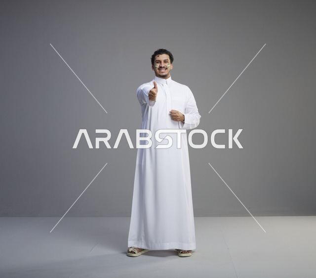 شاب سعودي بالثوب يرفع إبهامه احتفالاً باليوم الوطني