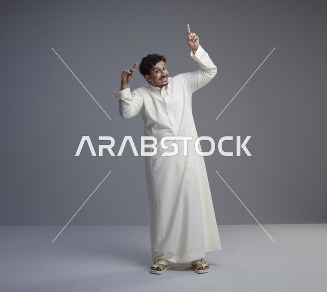 رجل سعودي بالثوب التقليدي الأبيض يشير للأعلى في استوديو