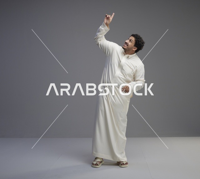رجل سعودي بالثوب الأبيض يشير للأعلى في استوديو