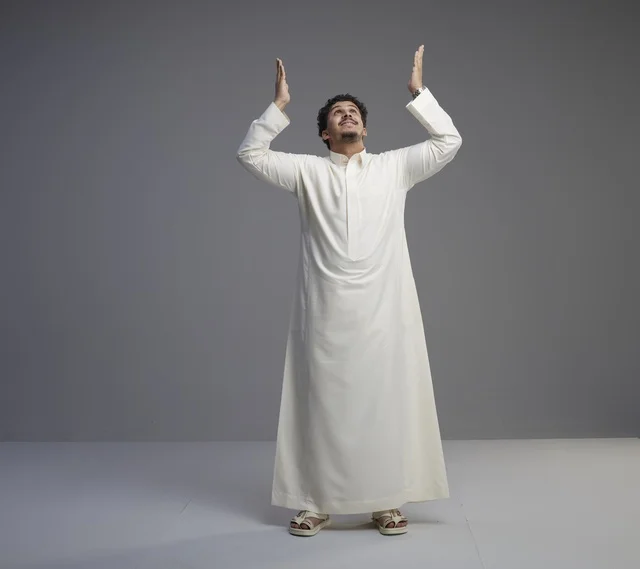 Saudi Man in White Thobe Praying Against Gray Background