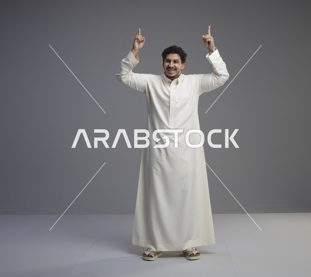 رجل سعودي بالثوب الأبيض يشير للأعلى بخلفية رمادية