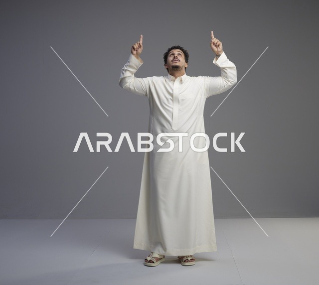 رجل سعودي بالثوب الأبيض يشير للأعلى في استوديو