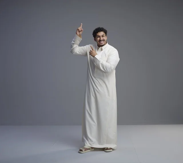 رجل سعودي بالثوب الأبيض يشير للأعلى في استوديو