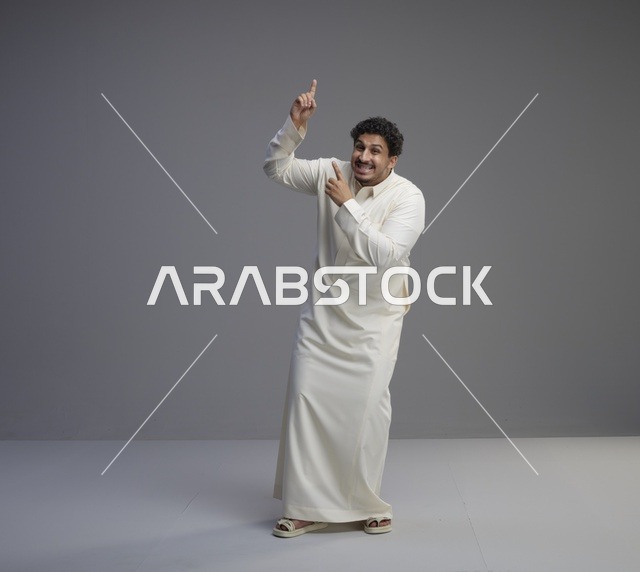 رجل سعودي بالثوب الأبيض يشير للأعلى في استوديو