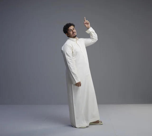 رجل سعودي يرتدي الثوب الأبيض التقليدي يشير للأعلى