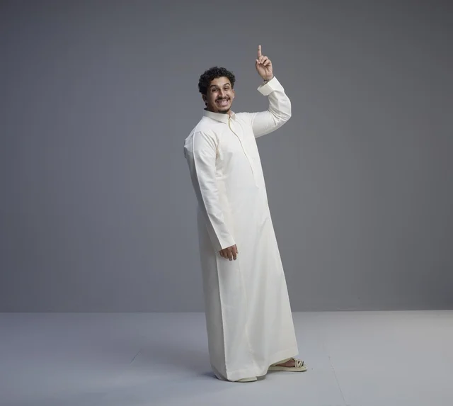 رجل سعودي يرتدي الثوب التقليدي يشير للأعلى في استوديو