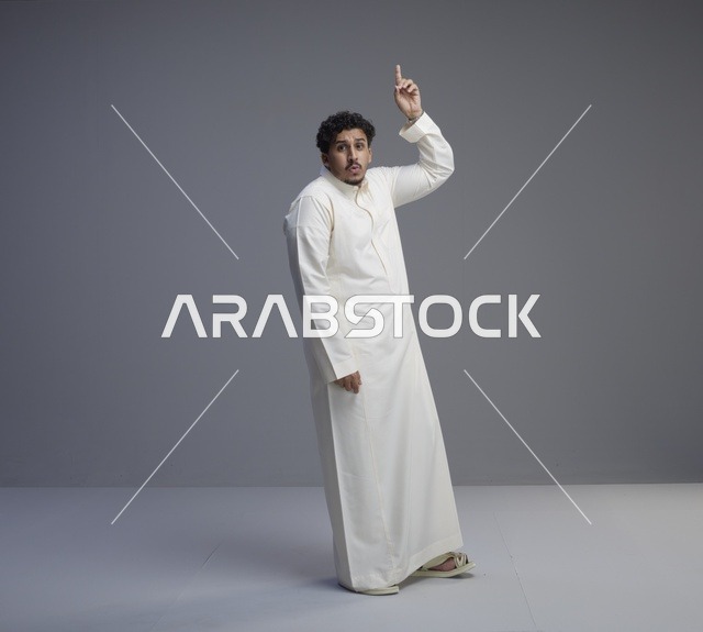 رجل سعودي بالثوب الأبيض يشير للأعلى في استوديو