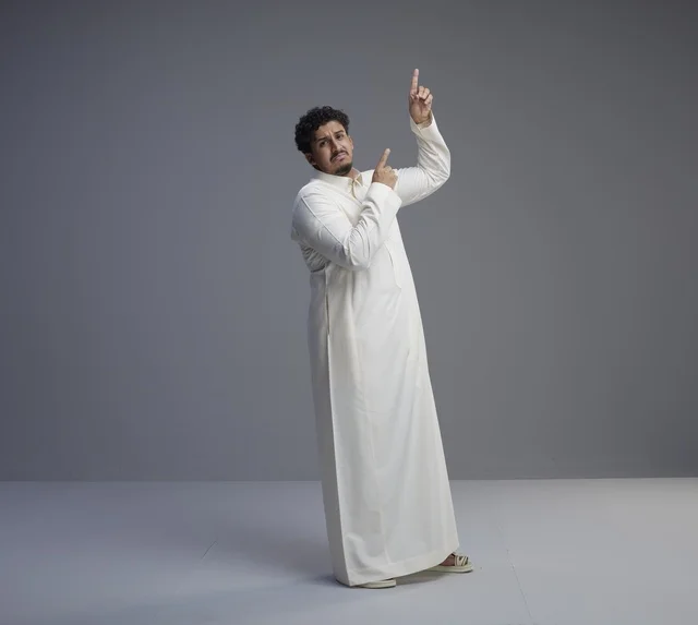 رجل سعودي بالثوب الأبيض يشير للأعلى في استوديو