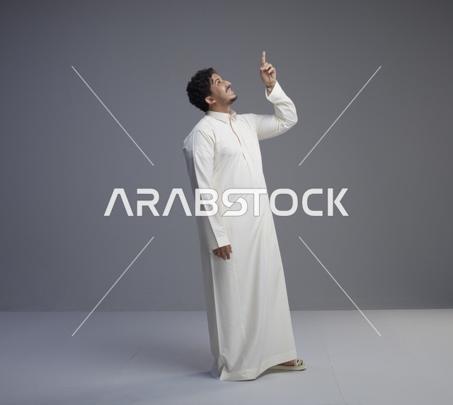 رجل سعودي يرتدي الثوب الأبيض ويشير للأعلى في استوديو
