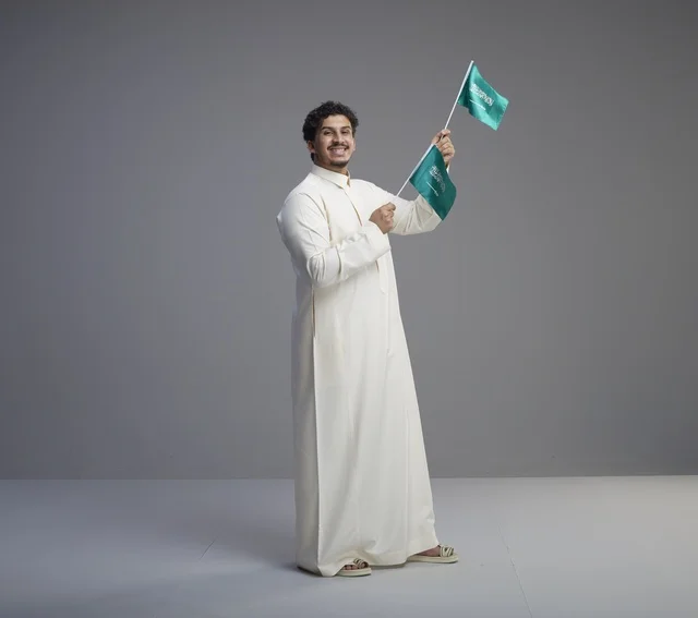 شاب سعودي يبتسم ويحمل علم المملكة العربية السعودية في استوديو