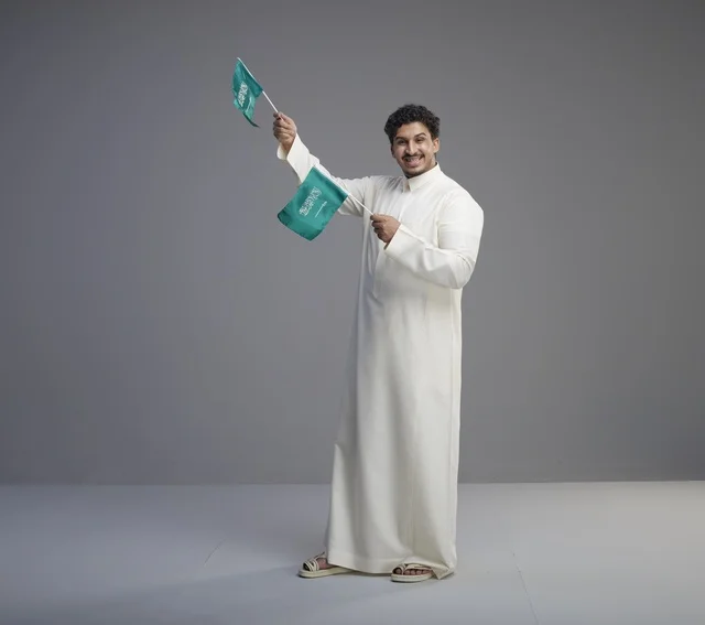 شاب سعودي مبتسم يلوح بعلم السعودية في الاستوديو